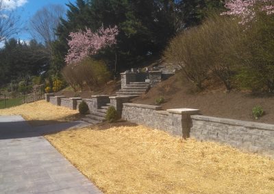 Interlocking stone retaining wall with stairs to an elevated fire pit